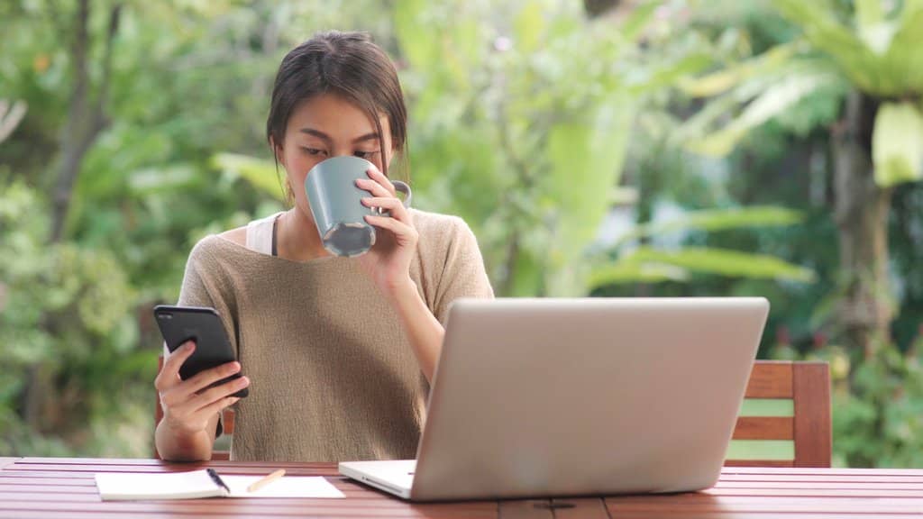 woman checking on her smartphone while working with laptop